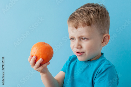 Little Boy Holding an Orange in his hands on blue background, diet and exercise for good health concept