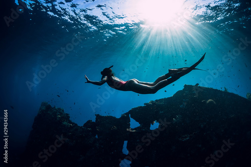 Obraz na plátně Free diver girl in pink swimwear with fins swimming underwater at wreck ship