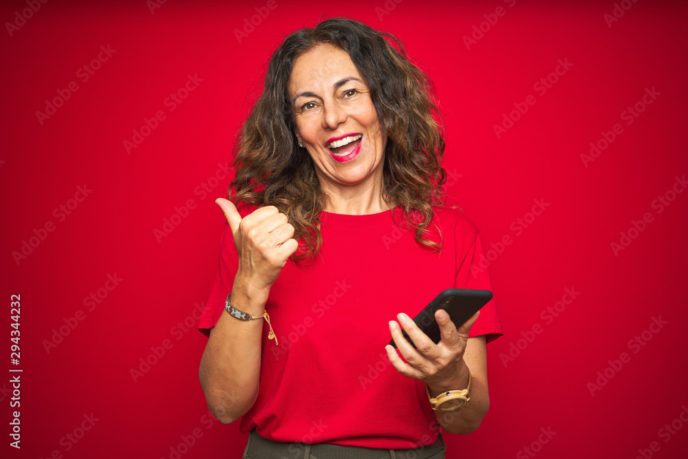 Naklejka premium Middle age senior woman using smartphone over red isolated background pointing and showing with thumb up to the side with happy face smiling