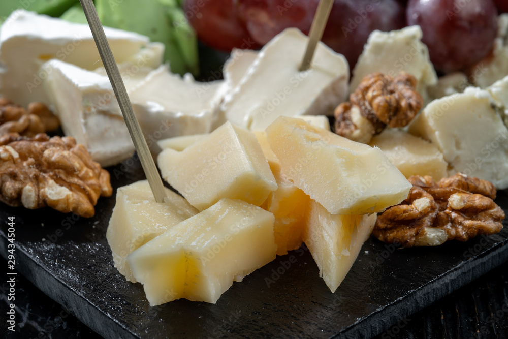 Plate with cheeses, grapes, walnuts. Laid out on black slate. Plate with cheeses, grapes, walnuts. Laid out on black slate.