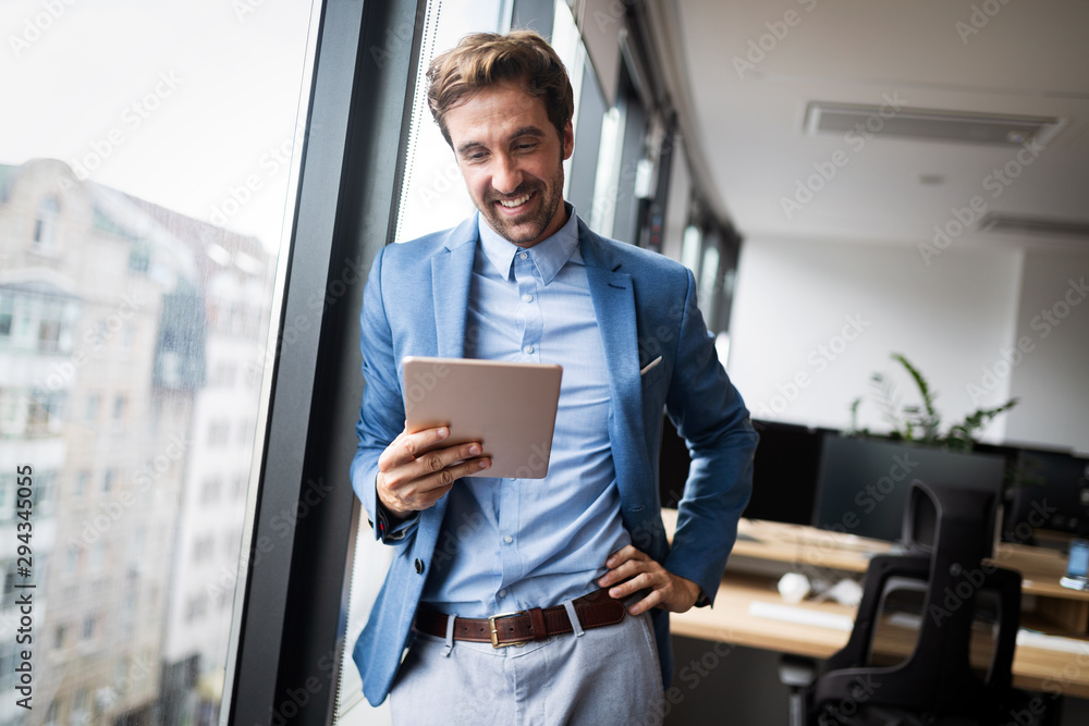 Portrait of young businessman smiling while using digital tablet in office