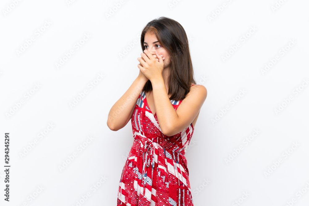 Caucasian girl in red dress over isolated white wall covering mouth and looking to the side Caucasian girl in red dress over isolated white wall covering mouth and looking to the side
