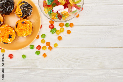 top view of colorful gummy sweets, bonbons and cupcakes on white wooden table, Halloween treat