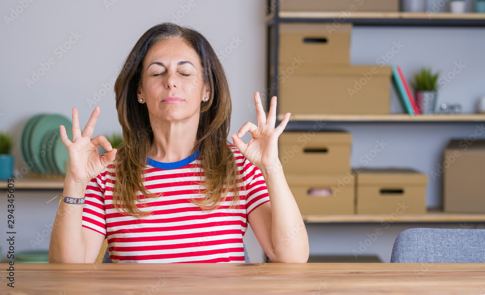 Middle age senior woman sitting at the table at home relaxed and smiling with eyes closed doing meditation gesture with fingers. Yoga concept. Middle age senior woman sitting at the table at home relaxed and smiling with eyes closed doing meditation gesture with fingers. Yoga concept.