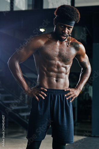 Portrait of tired swearty heavy breathing shirtless sportsman standing with hands on his hips and looking at camera