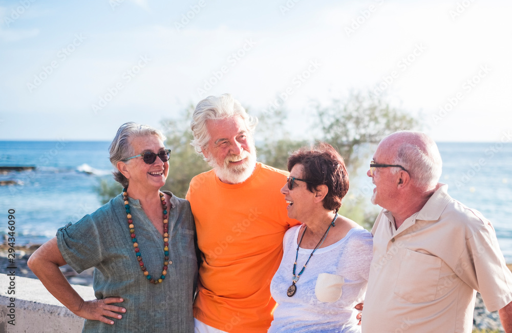 group of four senior and mature people with a friendship at the beach talking and enjoying together - sea at the background - obrazy, fototapety, plakaty 