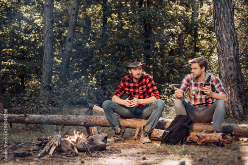 Good day for spring picnic in nature. Friends relaxing near campfire after day hiking or gathering mushrooms. Two Happy people sitting around campfire with beer.