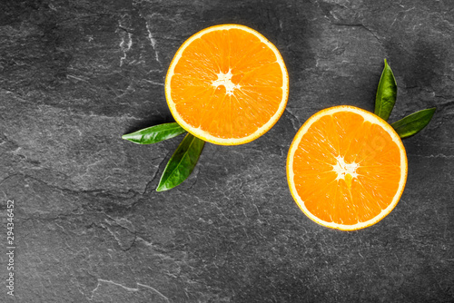 Oranges on dark stone table. Fresh orange fruits on table top view. Half oranges with green leaves. © Milan
