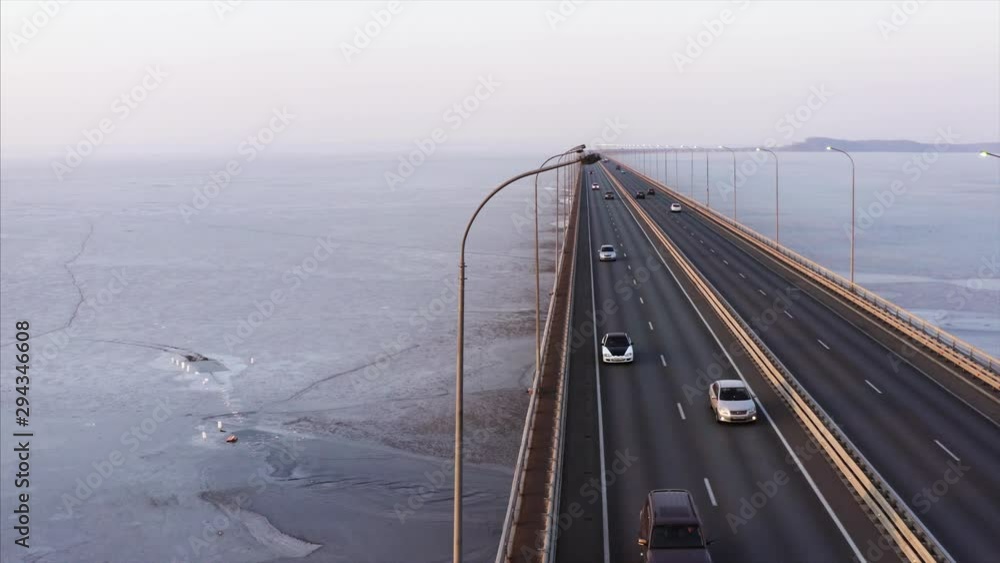 Flying sideways above low water bridge with driving cars across frozen Amur Bay of Far East of Russia. Aerial view. Evening Flying sideways above low water bridge with driving cars across frozen Amur Bay of Far East of Russia. Aerial view. Evening