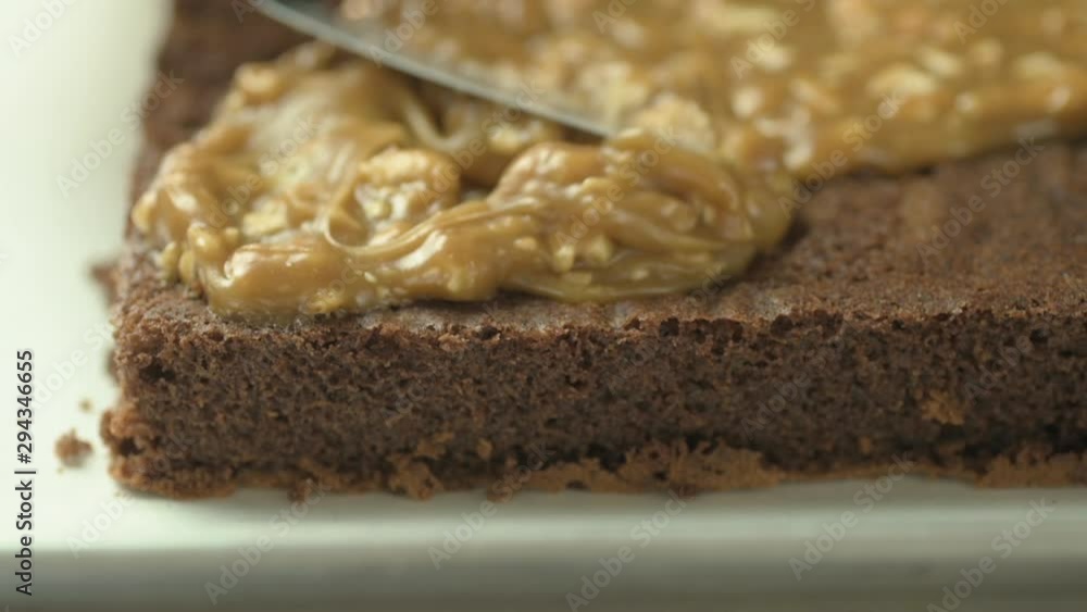 Close up on spatula spreading caramel and nuts on top of a chocolate sponge cake. Close up on spatula spreading caramel and nuts on top of a chocolate sponge cake.