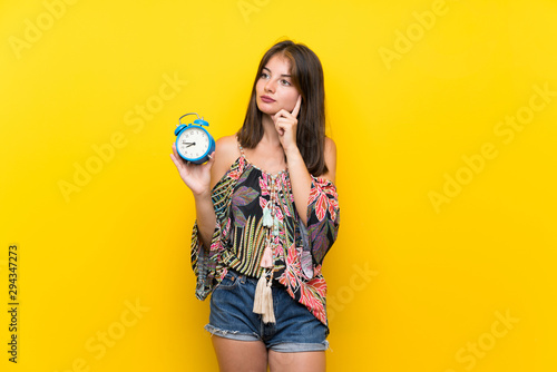 Caucasian girl in colorful dress over isolated yellow background holding vintage alarm clock © luismolinero