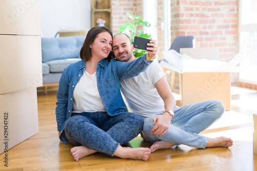 Young couple taking a picture photo using smartphone at new home, sitting on the floor smiling happy for moving to new apartment