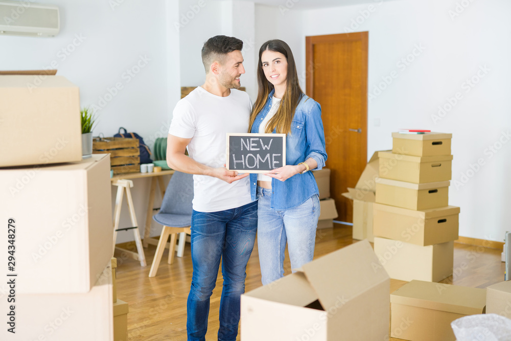 Beautiful young couple moving to a new house, smiling very happy holding blackboard with new home text Beautiful young couple moving to a new house, smiling very happy holding blackboard with new home text