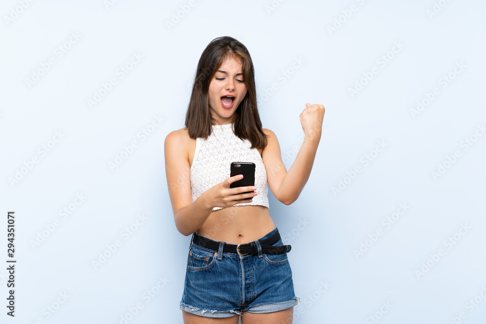Young woman over isolated blue background with phone in victory position Young woman over isolated blue background with phone in victory position