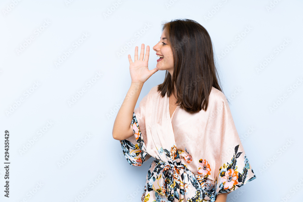 Caucasian girl with kimono over isolated blue background shouting with mouth wide open Caucasian girl with kimono over isolated blue background shouting with mouth wide open