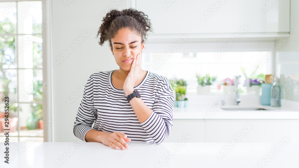 Beautiful african american woman with afro hair wearing casual striped sweater touching mouth with hand with painful expression because of toothache or dental illness on teeth. Dentist concept. Beautiful african american woman with afro hair wearing casual striped sweater touching mouth with hand with painful expression because of toothache or dental illness on teeth. Dentist concept.