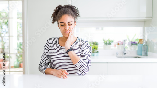 Beautiful african american woman with afro hair wearing casual striped sweater touching mouth with hand with painful expression because of toothache or dental illness on teeth. Dentist concept.