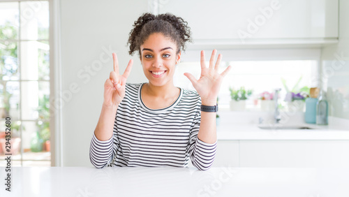 Beautiful african american woman with afro hair wearing casual striped sweater showing and pointing up with fingers number seven while smiling confident and happy.