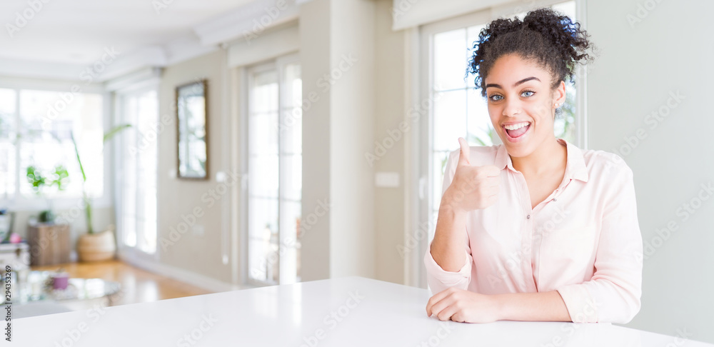 Wide angle of beautiful african american woman with afro hair doing happy thumbs up gesture with hand. Approving expression looking at the camera showing success.