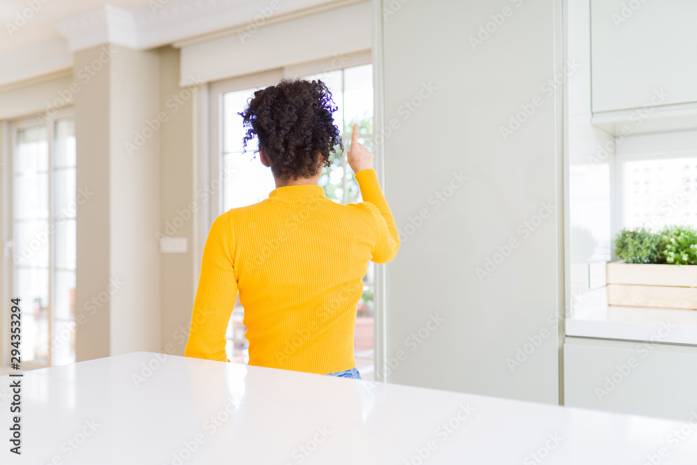 Beautiful african american woman with afro hair wearing a casual yellow sweater Posing backwards pointing ahead with finger hand