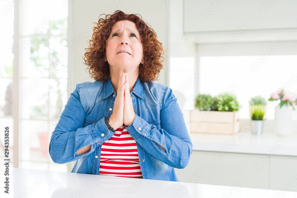 Middle age senior woman with curly hair wearing denim jacket at home begging and praying with hands together with hope expression on face very emotional and worried. Asking for forgiveness Middle age senior woman with curly hair wearing denim jacket at home begging and praying with hands together with hope expression on face very emotional and worried. Asking for forgiveness