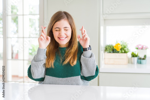 Young beautiful plus size woman wearing casual striped sweater gesturing finger crossed smiling with hope and eyes closed. Luck and superstitious concept.