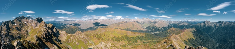 Aerial drone wide panoramic view of Caucasus mountains; rocky steep slopes, alpine meadows and snow fields; wild autumn nature, mixed forest and scenic skyline; place for hiking, tracking and tourism
