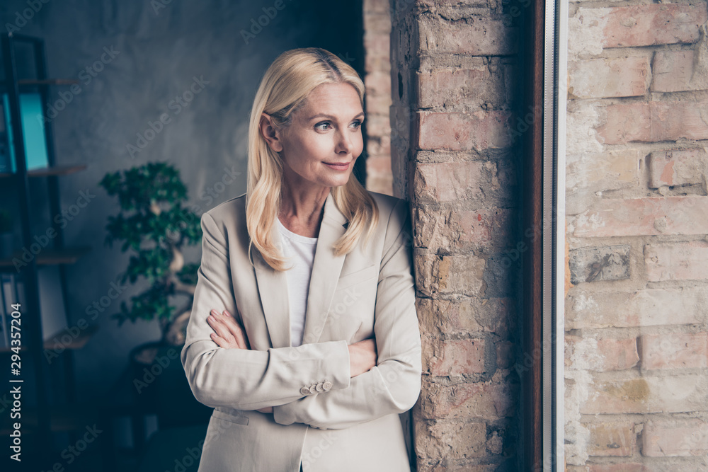 Portrait of dreamy thoughtful middle aged businesswoman cross her hands look in window think about her start-up future seminars for workers wear stylish jacket stand brick wall in office company Portrait of dreamy thoughtful middle aged businesswoman cross her hands look in window think about her start-up future seminars for workers wear stylish jacket stand brick wall in office company