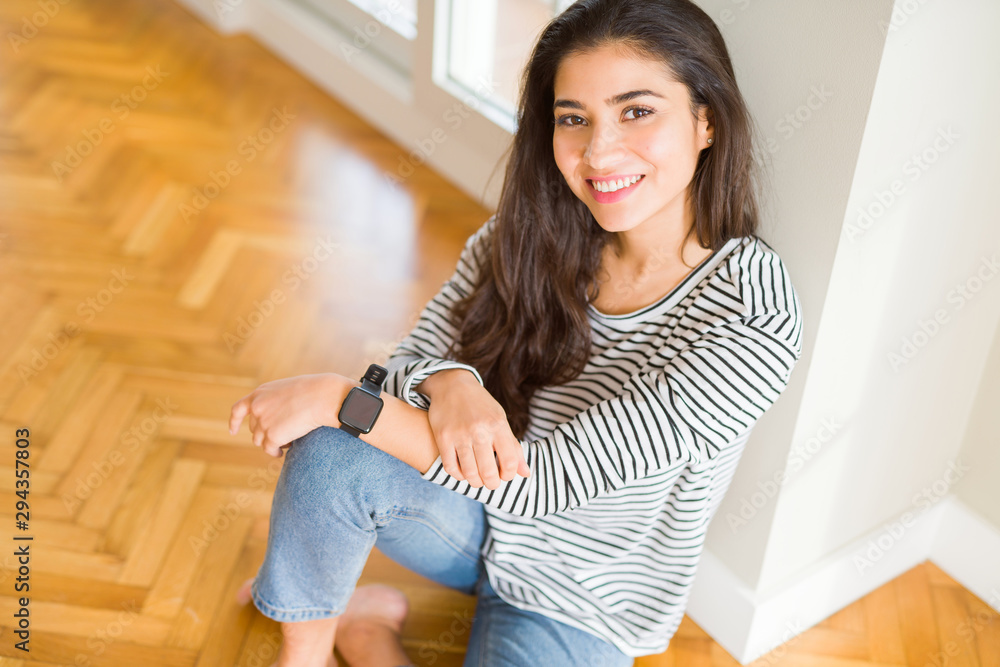 Beautiful brunette woman smiling cheerful with big smile, looking positive and happy with crossed arms sitting on the floor Beautiful brunette woman smiling cheerful with big smile, looking positive and happy with crossed arms sitting on the floor