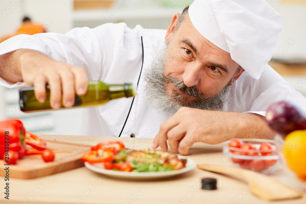 Close up portrait of professional senior chef decorating meat steak with olive oil and vegetables, copy space Close up portrait of professional senior chef decorating meat steak with olive oil and vegetables, copy space