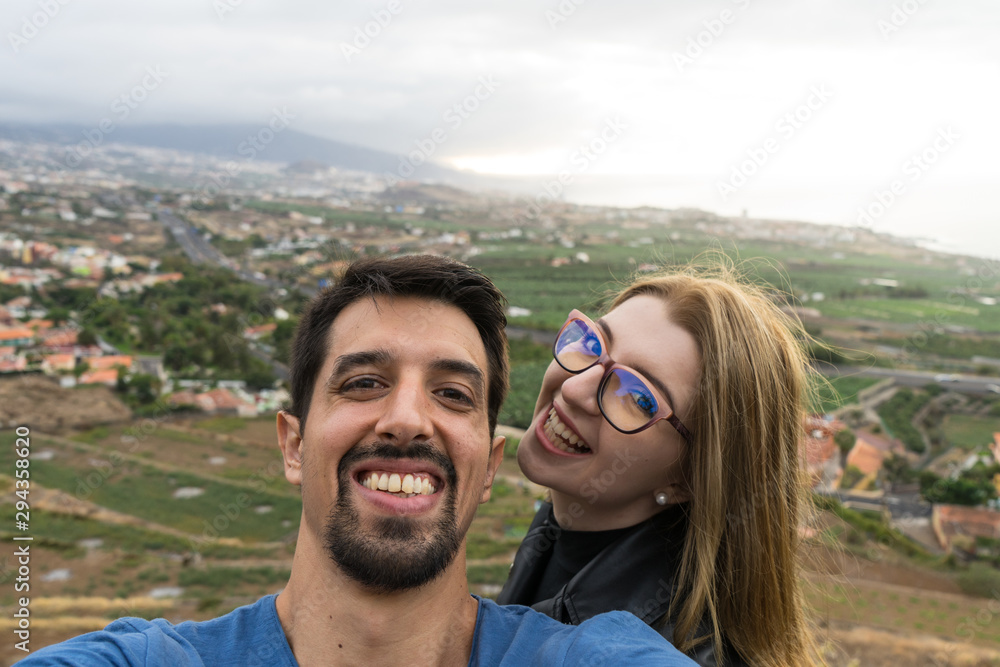 Joyful interracial Heterosexual Couple, Husband and Wife take a selfie looking at camera with affection, outside in honeymoon trip. Boyfriend and girlfriend with glasses, and romantic feelings.