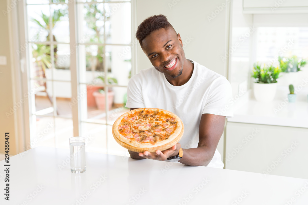 Handsome young african man holding and showing smiling proud homemade cheese pizza
