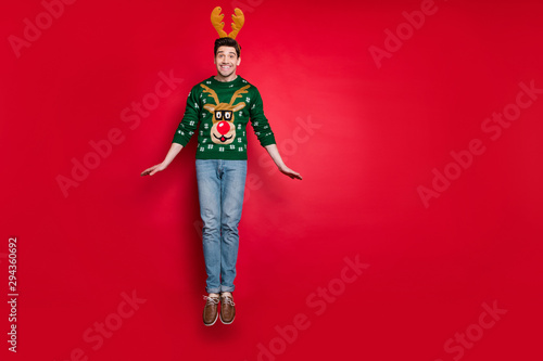 Full body photo of funky guy jumping high excited with x-mas discount prices wear knitted green pullover with ugly deer ornament isolated red color background