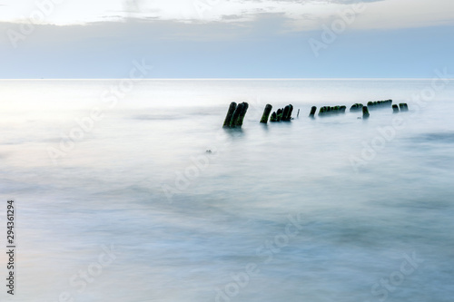long exposure smooth sea surface with breakwater sticking out of the water in blue twilight