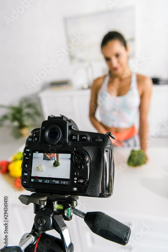 selective focus of digital camera with sportswoman gesturing near vegetables