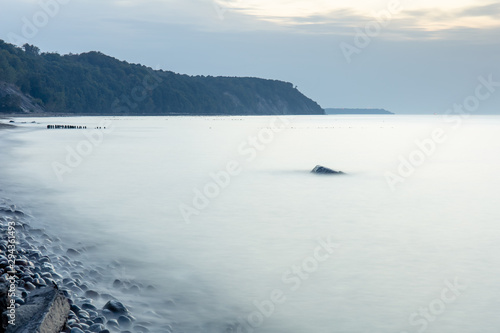 steep coastline on the horizon  smooth surface of the sea at a long exposure with a large stone sticking out of the water in twilight