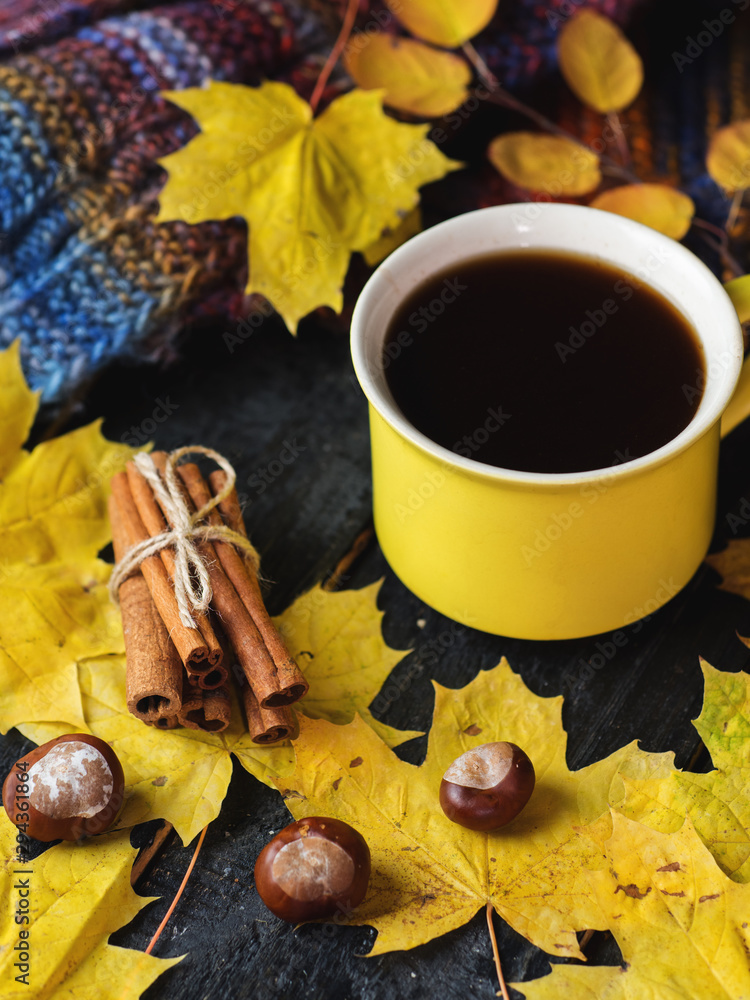 a yellow mug of coffee on the table with yellow autumn leaves and a knitted scarf . cozy home morning a yellow mug of coffee on the table with yellow autumn leaves and a knitted scarf . cozy home morning