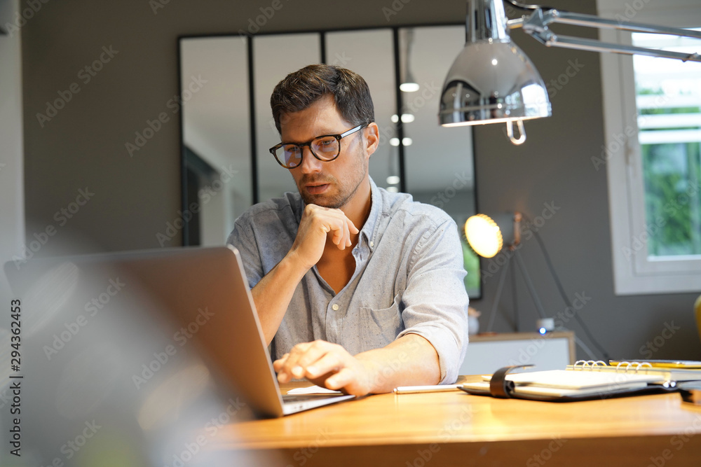 Middle-aged man working on laptop in office - obrazy, fototapety, plakaty 