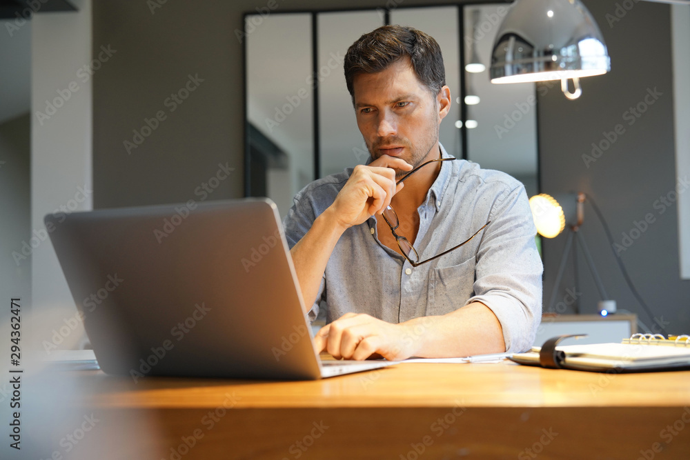 Middle-aged man working on laptop in office - obrazy, fototapety, plakaty 