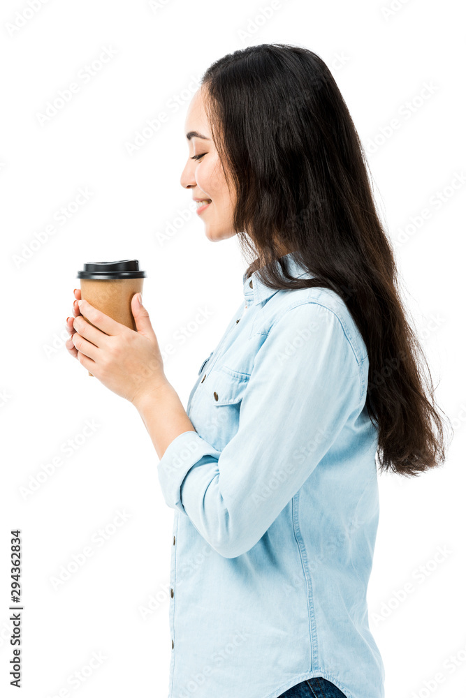 side view of attractive and smiling asian woman in denim shirt holding paper cup isolated on white side view of attractive and smiling asian woman in denim shirt holding paper cup isolated on white