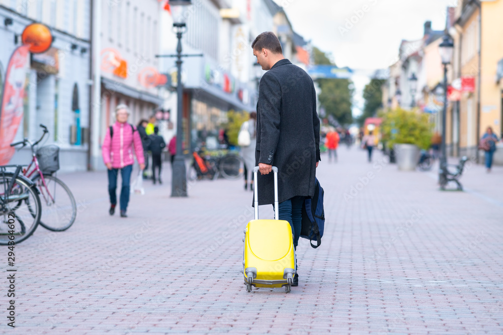 Young man wheeling a suitcase down a street