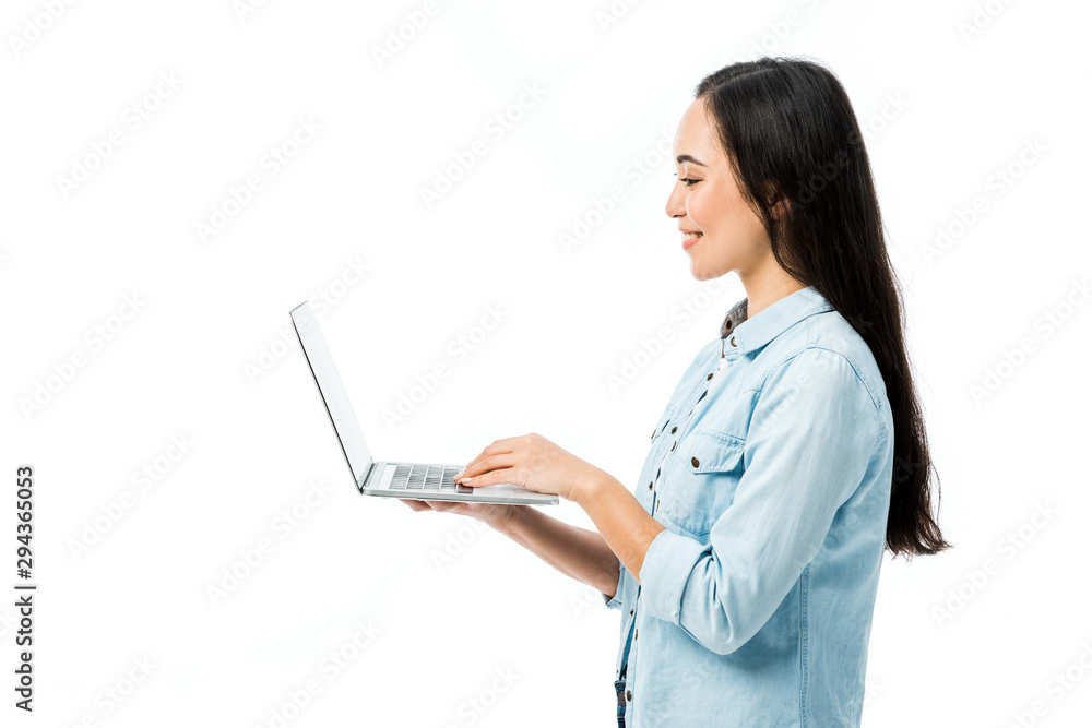 side view of attractive asian woman in denim shirt smiling and holding laptop isolated on white side view of attractive asian woman in denim shirt smiling and holding laptop isolated on white