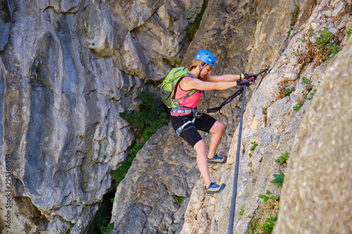 Tourist on via ferrata in Turda gorge (Cheile Turzii) Romania, crossing a traverse section, using straight arms and good climbing technique.
