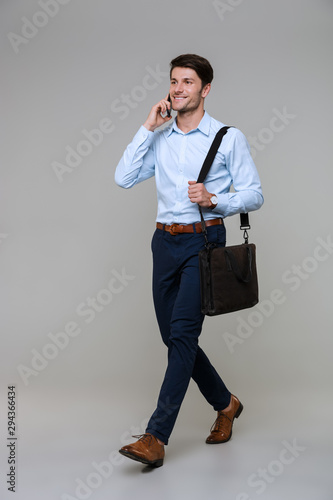 Full length portrait of businessman with laptop bag talking on smartphone