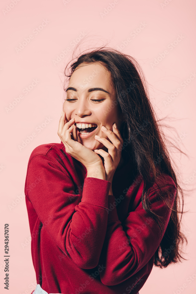 attractive asian woman with closed eyes in red sweater smiling isolated on pink attractive asian woman with closed eyes in red sweater smiling isolated on pink