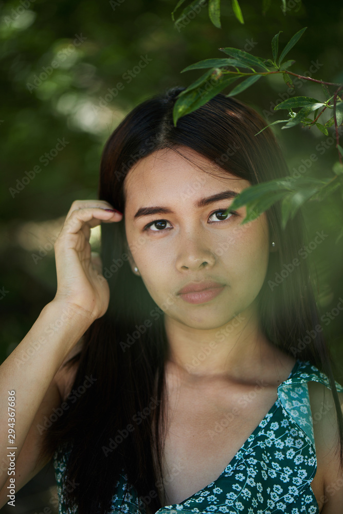 Horizontal natural beauty portrait of authentic thai asian young woman in summer dress in forest near green tree