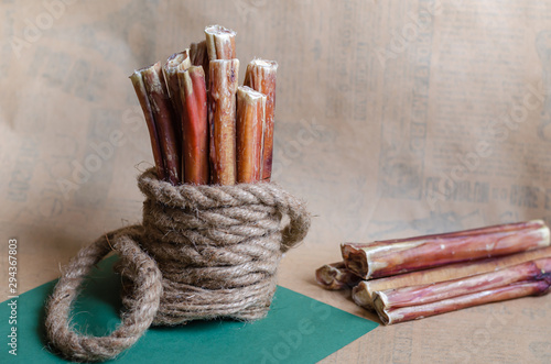 A group of several dried bully sticks on a textured light brown background. The stack is tied with a natural hemp rope. Close-up. Eye level shooting. Soft focus. Landscape orientation