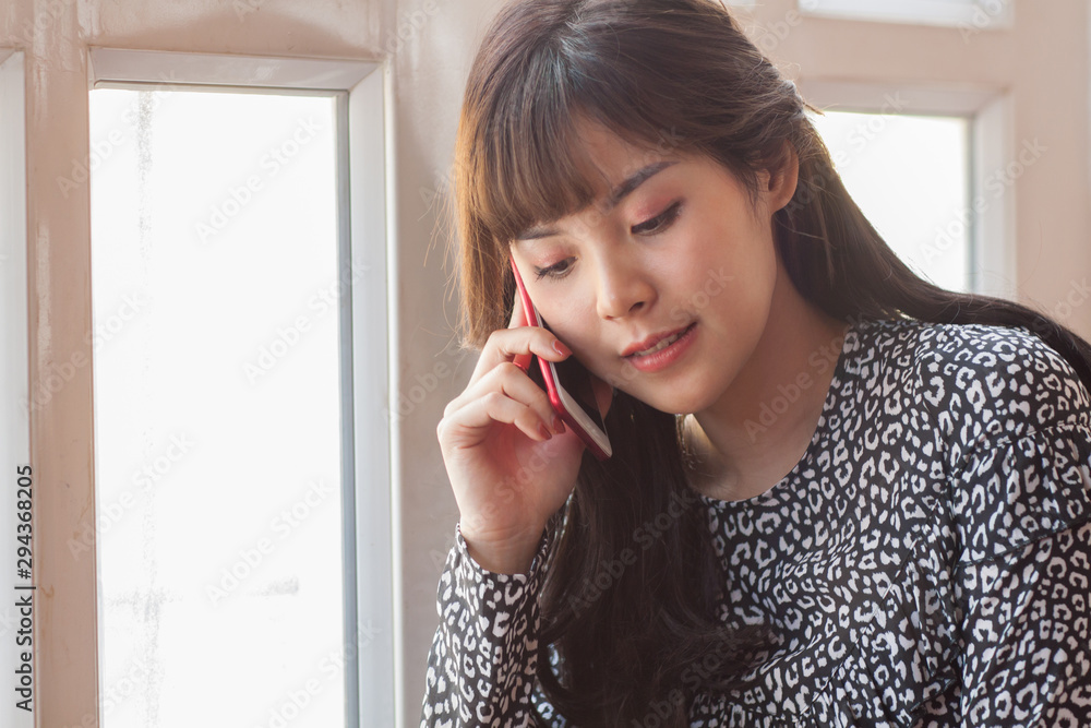 A cute Asian girl holds a phone and is happily talking to someone. Women are using mobile phones to talk to someone. Women are talking to someone via mobile phone.