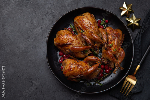 Fotografia Roasted quail with cranberry and thyme on black plate for Christmas dinner,