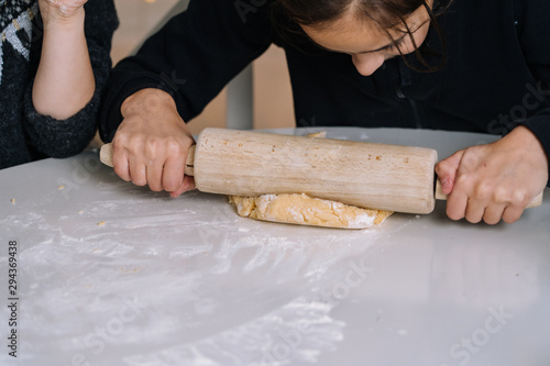 Detail of young kids baking Christmas gingerbread cookies in house kitchen on winter day. Child with rolling pin baking cookies. Baking and cooking with children for Christmas at home.Selective focus